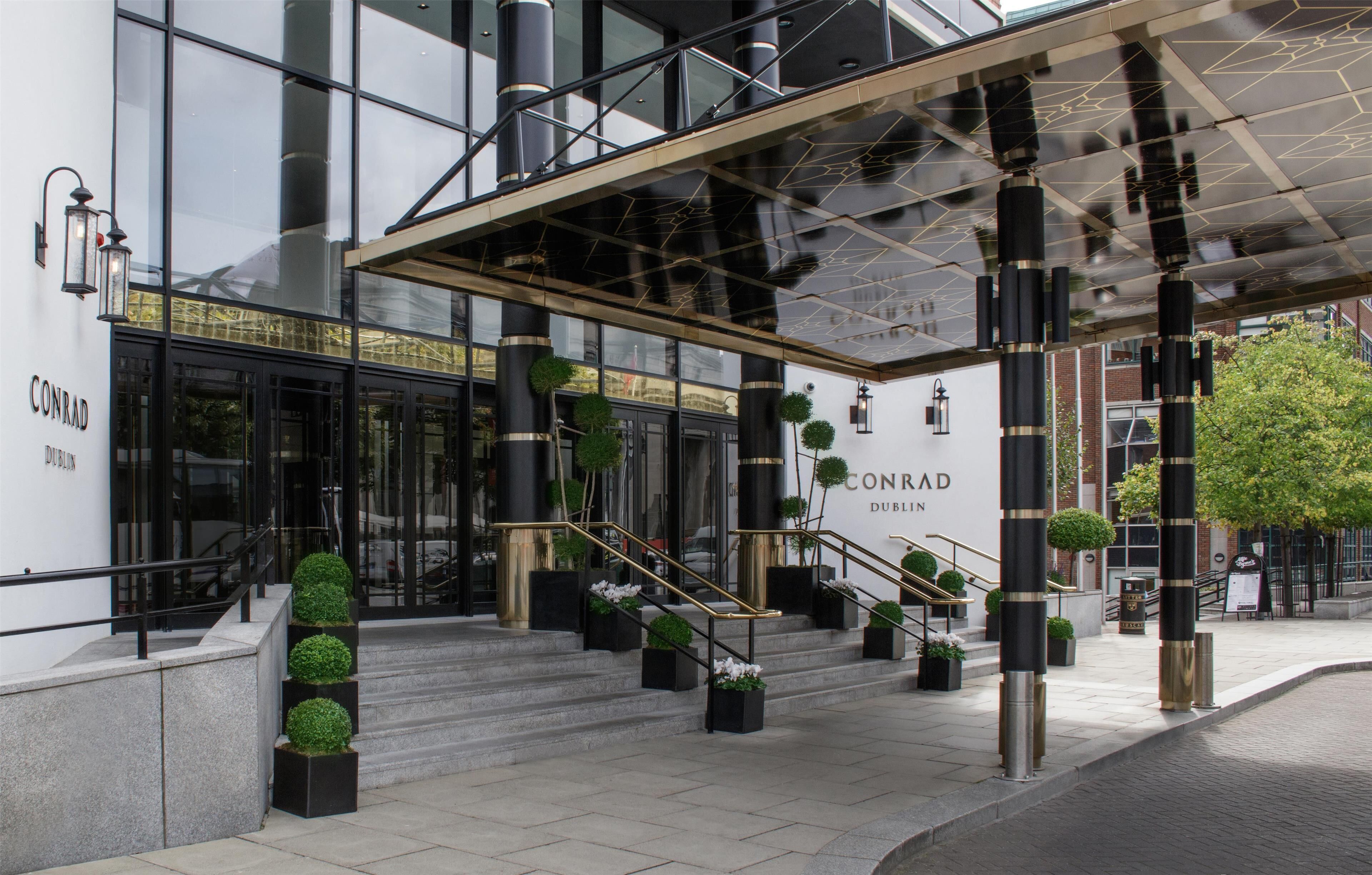 Ein Hotel mit Glasfassade, Stufen zum Eingang und schwarzen Poller.