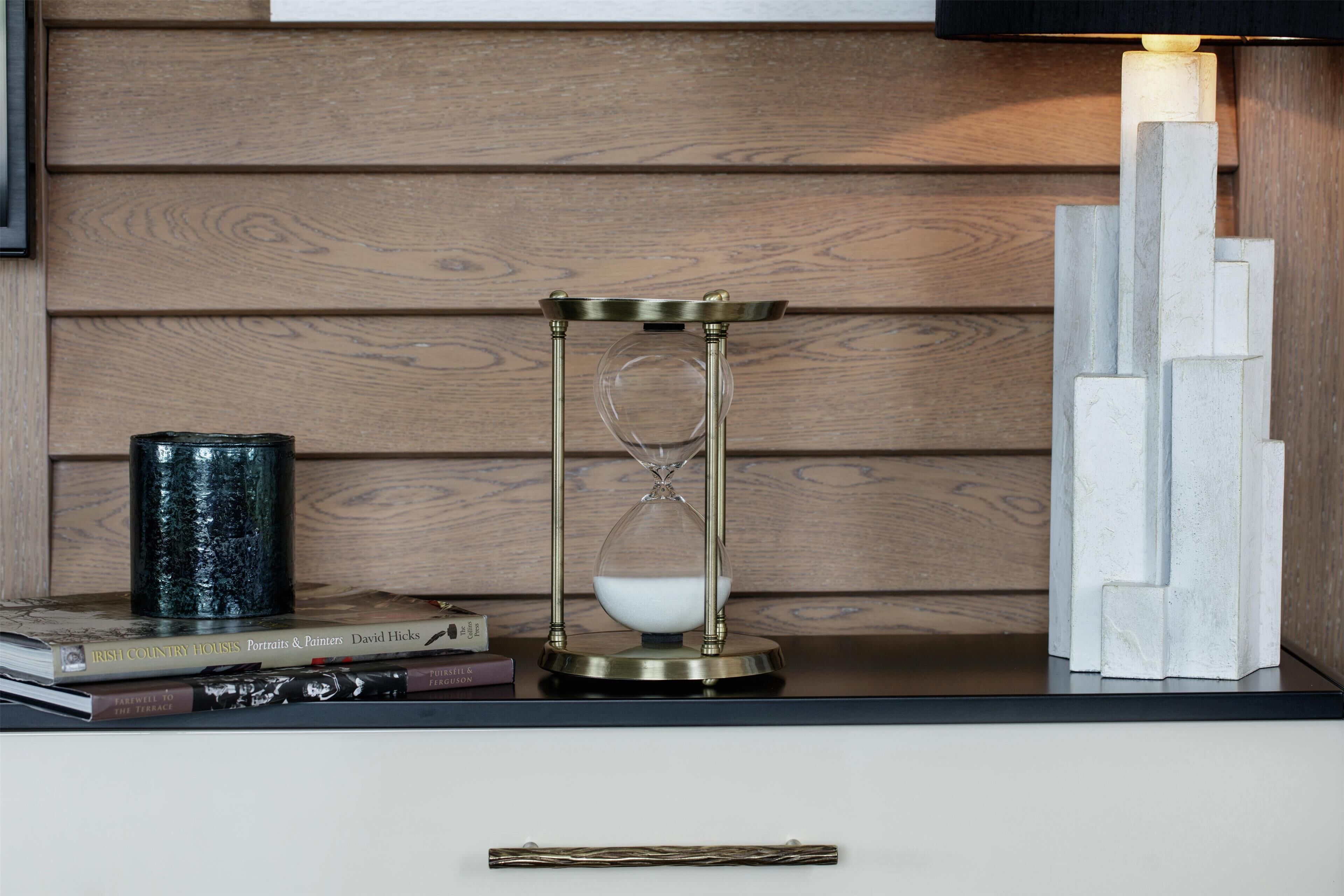 A wooden wall with a black lamp, a decorative hourglass, and a stack of books.