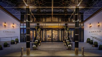 De ingang van hotel Conrad Dublin met een modern ontwerp, met grote pilaren, een geometrisch plafond en een uitnodigende trap.