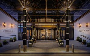 The entrance of Conrad Dublin hotel with a modern design, featuring large pillars, a geometric ceiling, and a welcoming staircase. - Conrad Dublin (Dublin)
