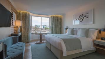 A hotel room with a large bed, a desk, a chair, a TV, and a window with curtains.