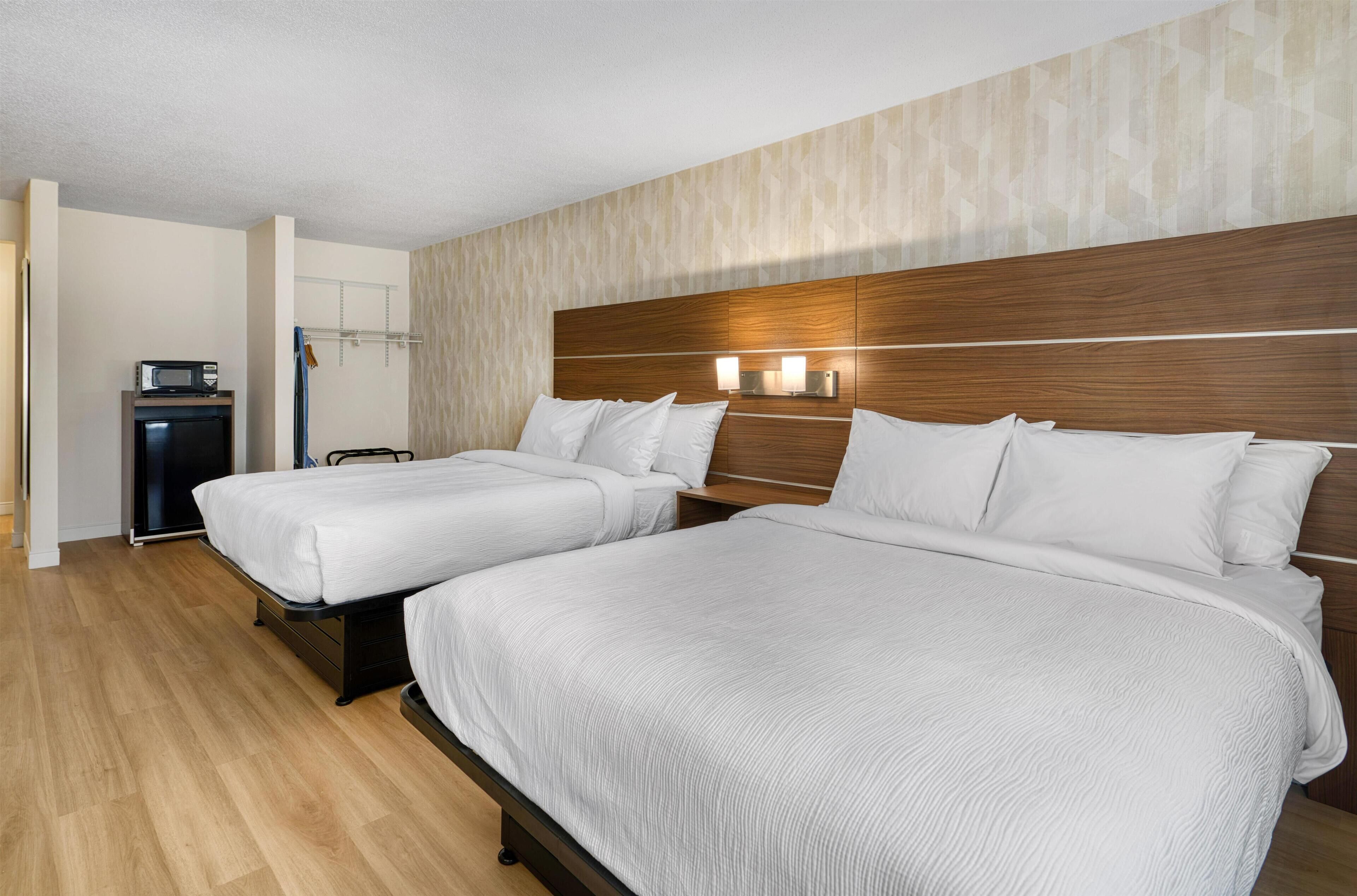 Een hotelkamer met twee bedden, een houten hoofdbord en een klein bureau met een magnetron.