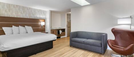 Quarto de hotel moderno com uma cama grande, um sofá cinzento, uma poltrona marrom e um claraboia.