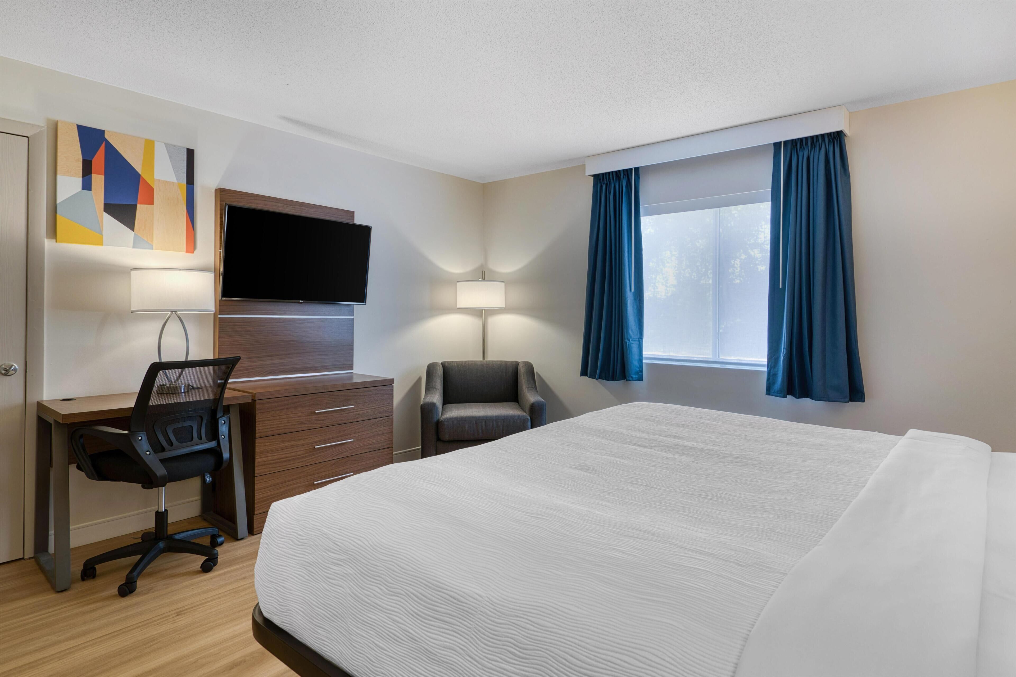Habitación de hotel con una cama grande, un escritorio con silla, televisor y ventana con cortinas.