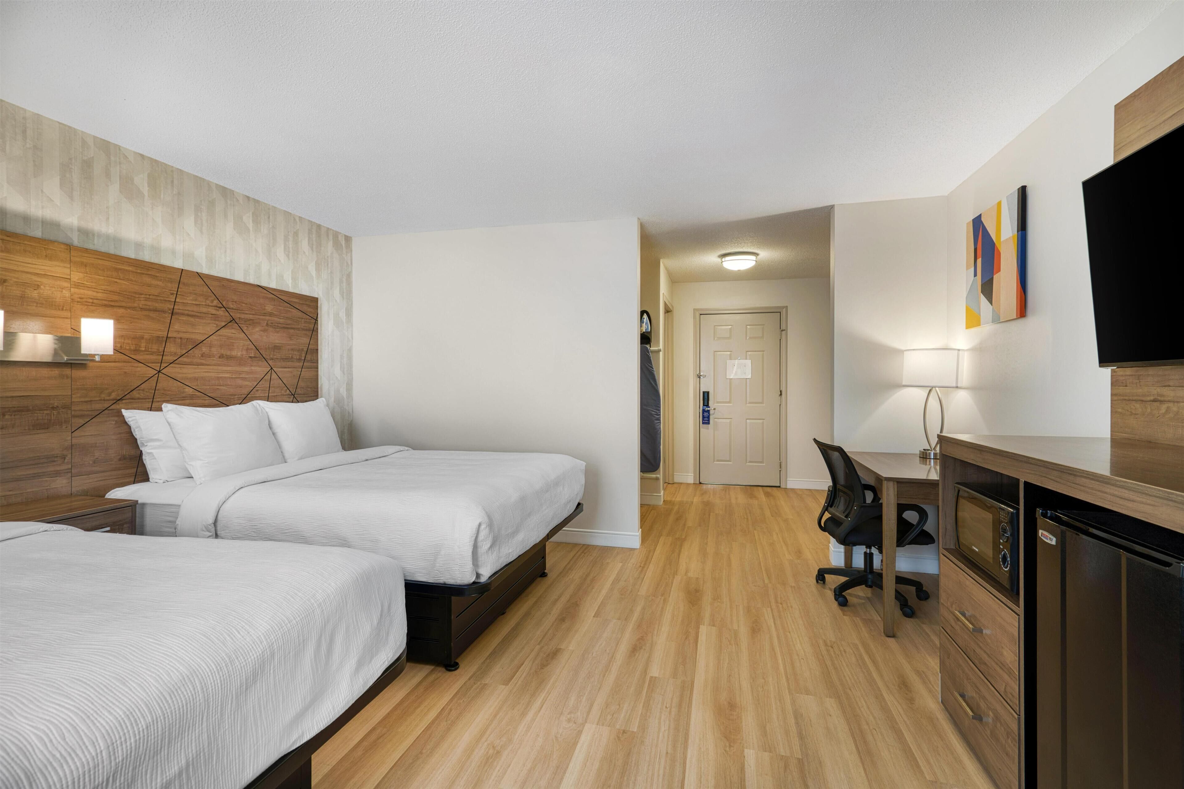 Habitación de hotel con dos camas, un escritorio, una silla, un televisor y una puerta que da a otra habitación.