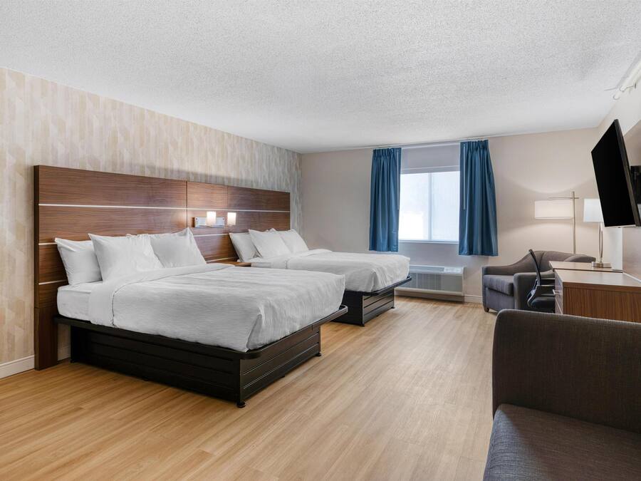 A hotel room with two beds, a desk, a chair, and a TV.