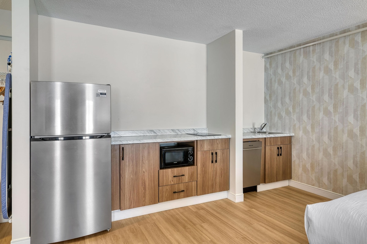 A compact kitchen with a stainless steel refrigerator, microwave, and dishwasher, wooden cabinets, and a marble countertop.