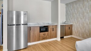 Una cocina compacta con refrigerador de acero inoxidable, microondas y lavavajillas, armarios de madera y encimera de mármol.