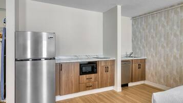 A compact kitchen with a stainless steel refrigerator, microwave, and dishwasher, wooden cabinets, and a marble countertop.