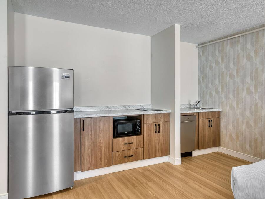 Eine kompakte Küche mit Edelstahl-Kühlschrank, Mikrowelle und Geschirrspüler, Holzschränken und einer Marmorarbeitsplatte.