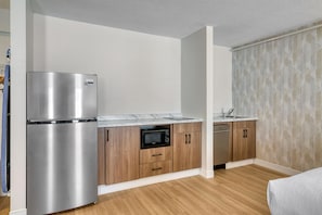 Una cocina compacta con refrigerador de acero inoxidable, microondas y lavavajillas, armarios de madera y encimera de mármol.