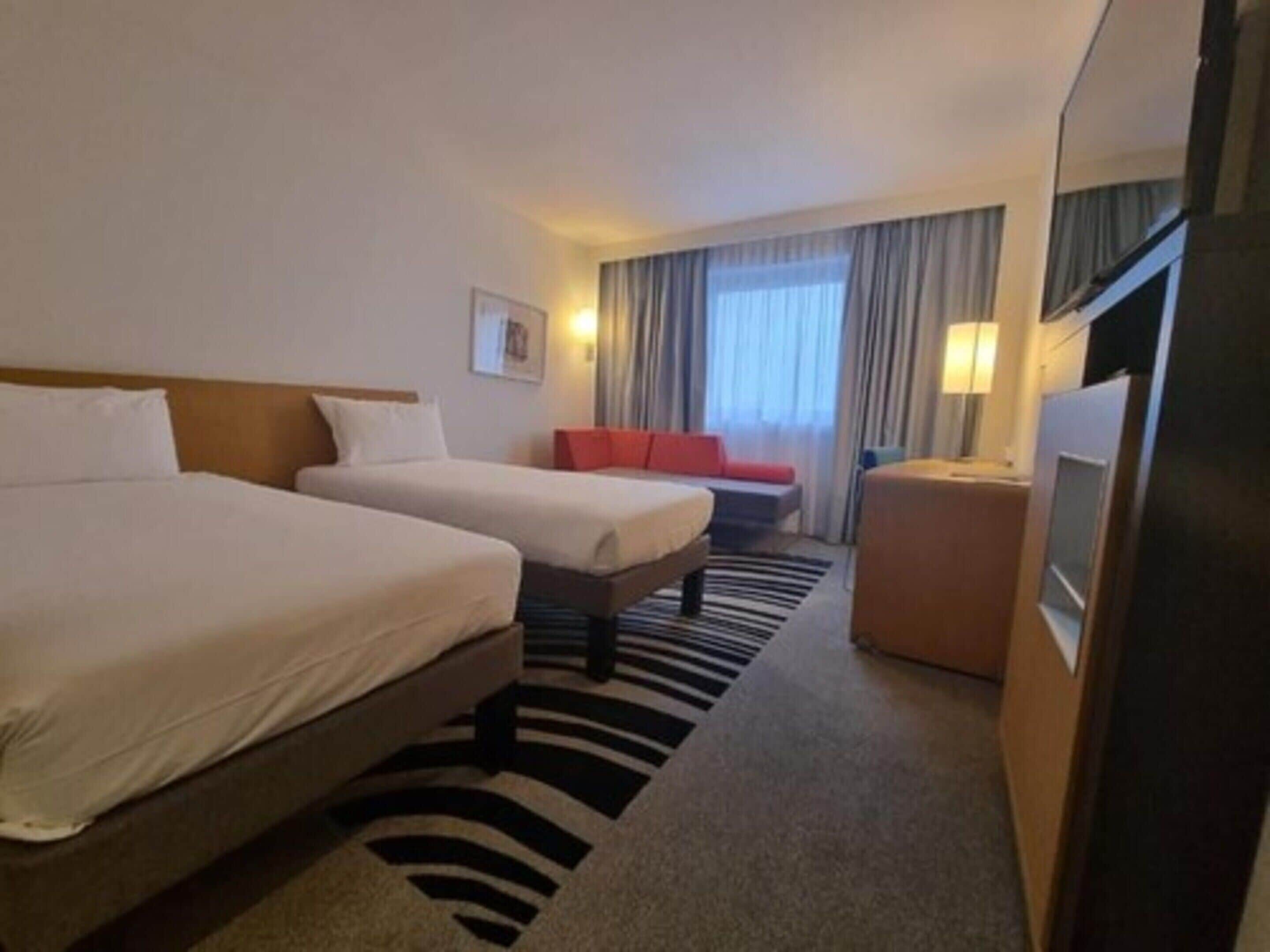A hotel room with two beds, a sofa, a TV, and a window with curtains.