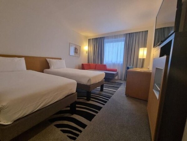 Une chambre d’hôtel avec deux lits, un canapé, une télévision et une fenêtre avec des rideaux.