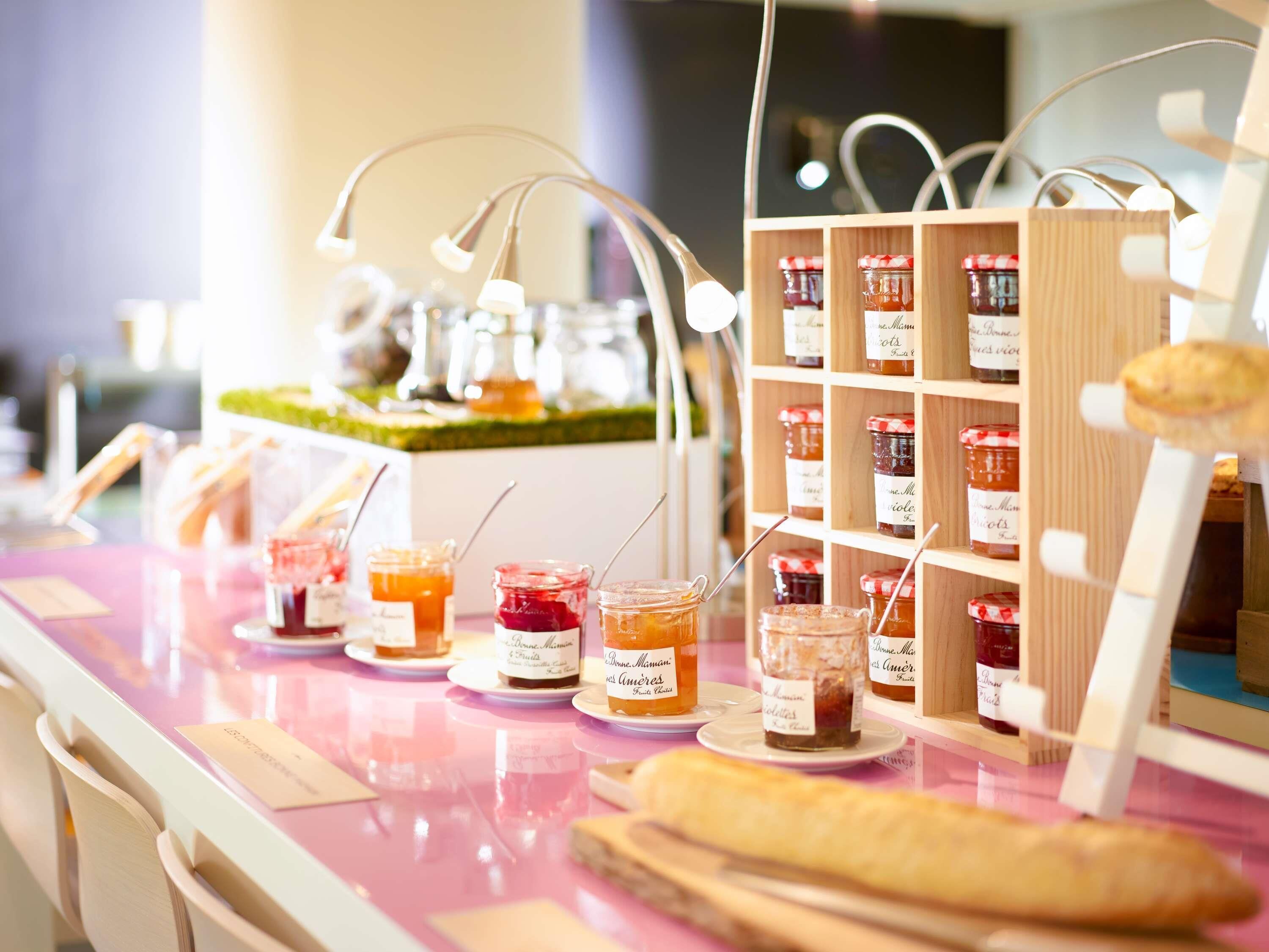 A food display with jars of preserves and a baguette on a pink table.