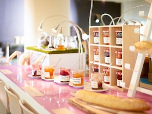 A food display with jars of preserves and a baguette on a pink table.