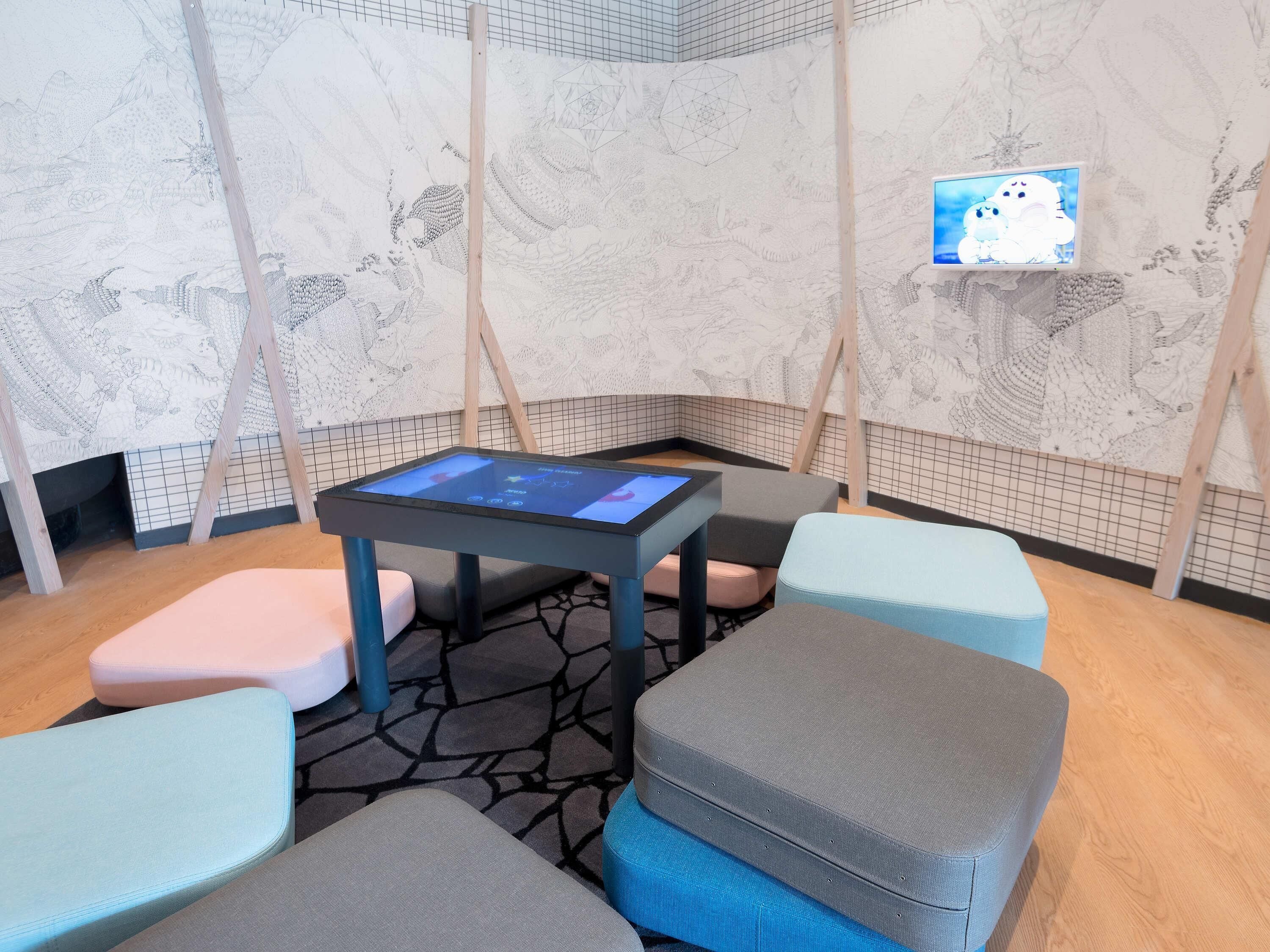 A room with a digital table displaying a game, cushioned seating, and patterned walls.