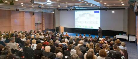 A conference room with a presentation screen, rows of chairs, and a stage with a podium.