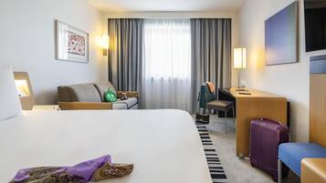 A hotel room with a bed, a desk, a chair, a suitcase, and a lamp.