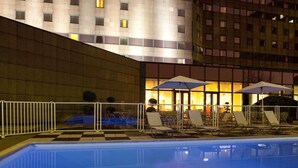 An outdoor swimming pool with lounge chairs and umbrellas, surrounded by a white fence. - Novotel Marne-La-Vallée Noisy-Le-Grand (Noisy-le-Grand)