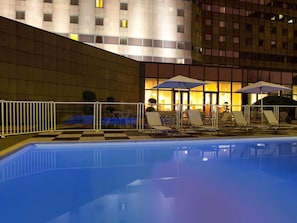 An outdoor swimming pool with lounge chairs and umbrellas, surrounded by a white fence.