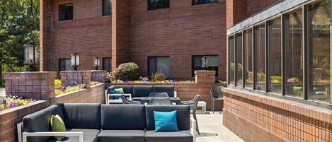 An outdoor patio with a sectional sofa, white chairs, and tables.