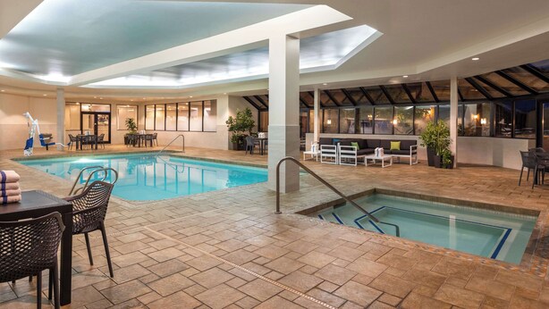 An indoor swimming pool with a sunroof, surrounded by seating areas and a bar. - Hampton by Hilton Spokane (Spokane)