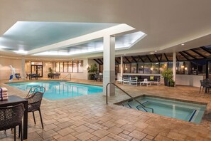 An indoor swimming pool with a sunroof, surrounded by seating areas and a bar.