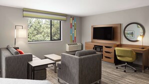 A hotel room with a sofa, a desk, a chair, a TV, a mirror, and a window with a view of trees. - Hampton by Hilton Spokane (Spokane)