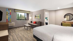 A hotel room with a large bed, a sofa, a small table, a TV, and a window with a view of trees. - Hampton by Hilton Spokane (Spokane)