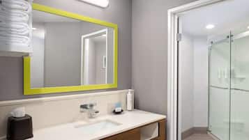 A modern bathroom with a large mirror, a sink, and a glass shower enclosure.