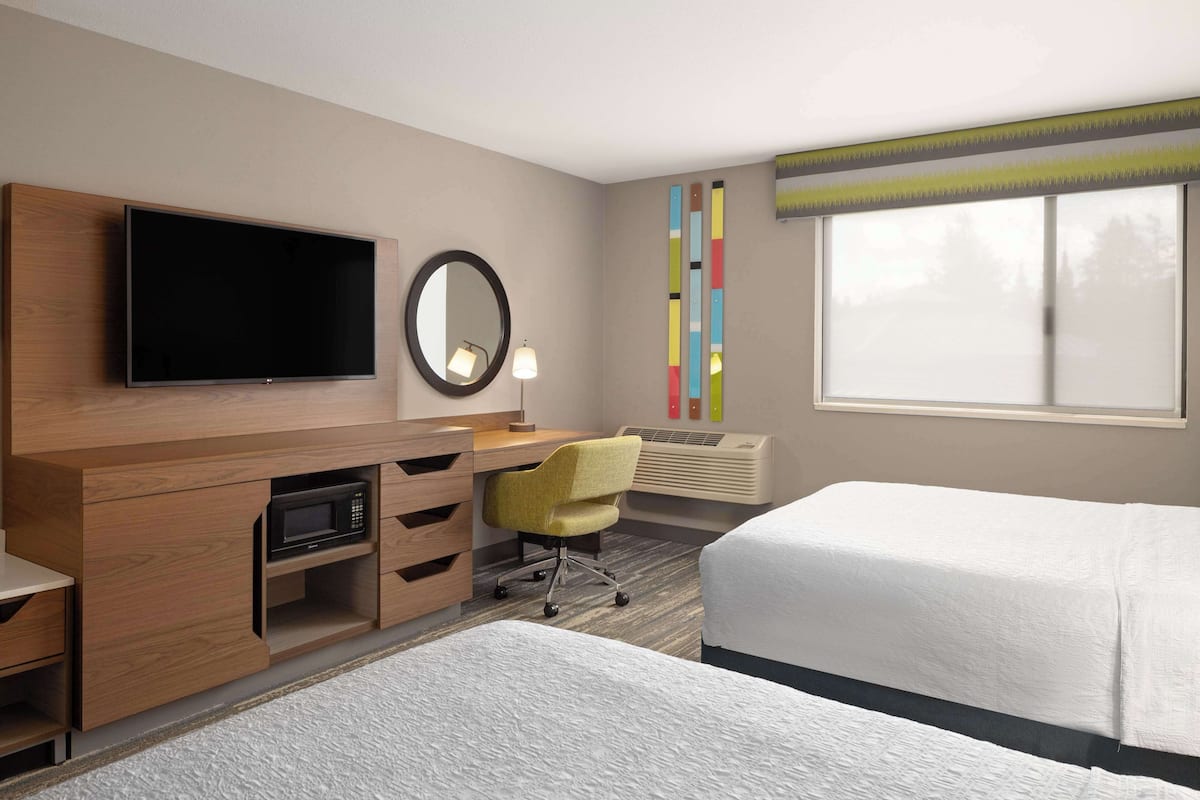 A hotel room with a flat-screen TV, a desk with a chair, a bed, and a large window.
