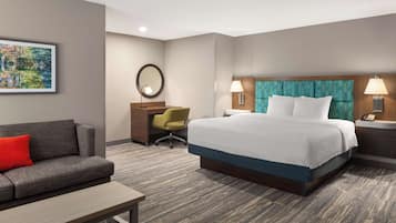 A hotel room with a bed, a desk, a chair, a sofa, and a painting on the wall.