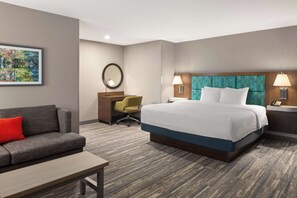 A hotel room with a bed, a desk, a chair, a sofa, and a painting on the wall.