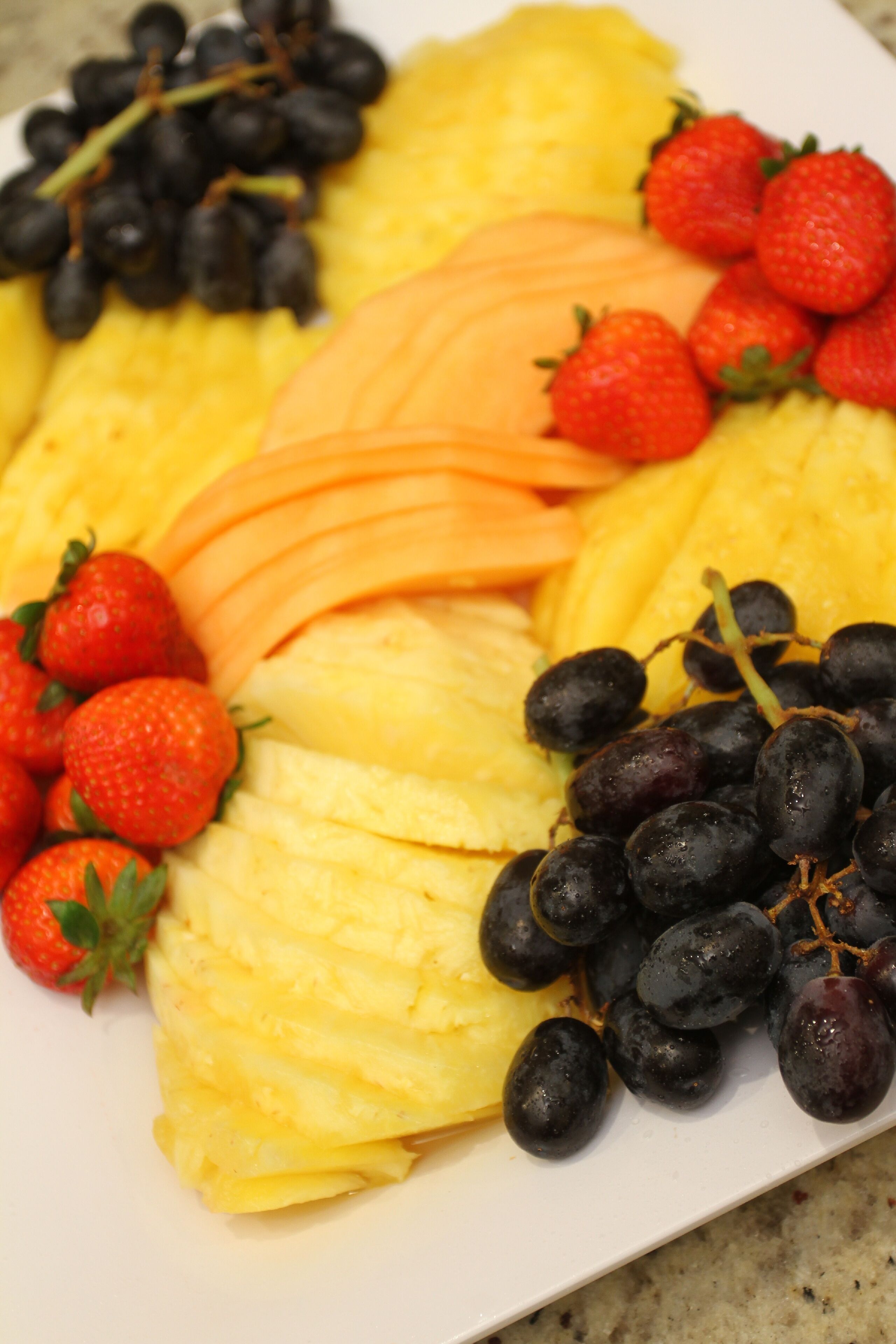 Una bandeja de frutas con piña, uvas y fresas.
