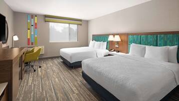 A hotel room with two beds, a desk, a chair, and a large window.