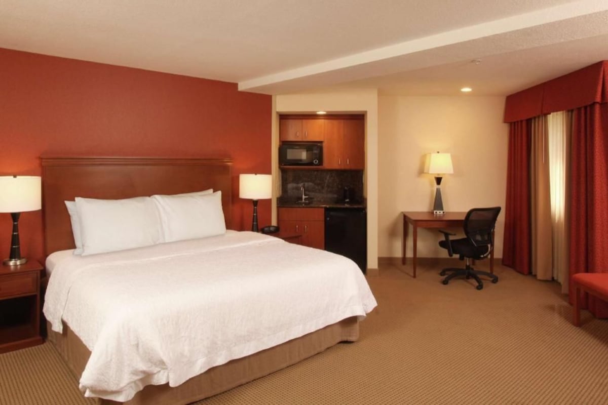 A hotel room with a bed, a desk, a chair, a microwave, and a small kitchenette.