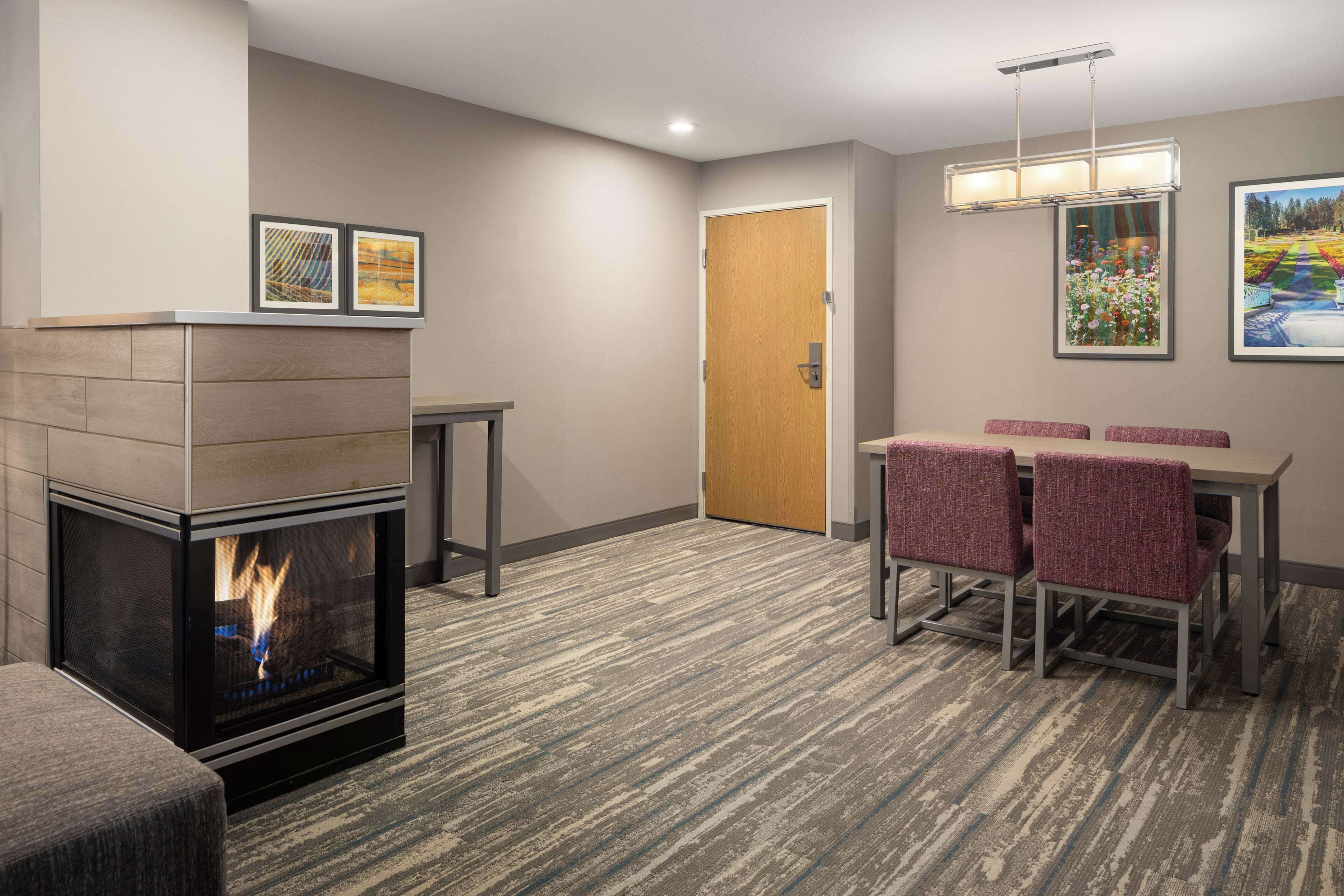 Una habitación de hotel con chimenea, una zona de comedor con cuatro sillas, una mesa y obras de arte en las paredes.