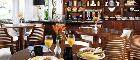 A breakfast setting with round tables, chairs, and a buffet counter.