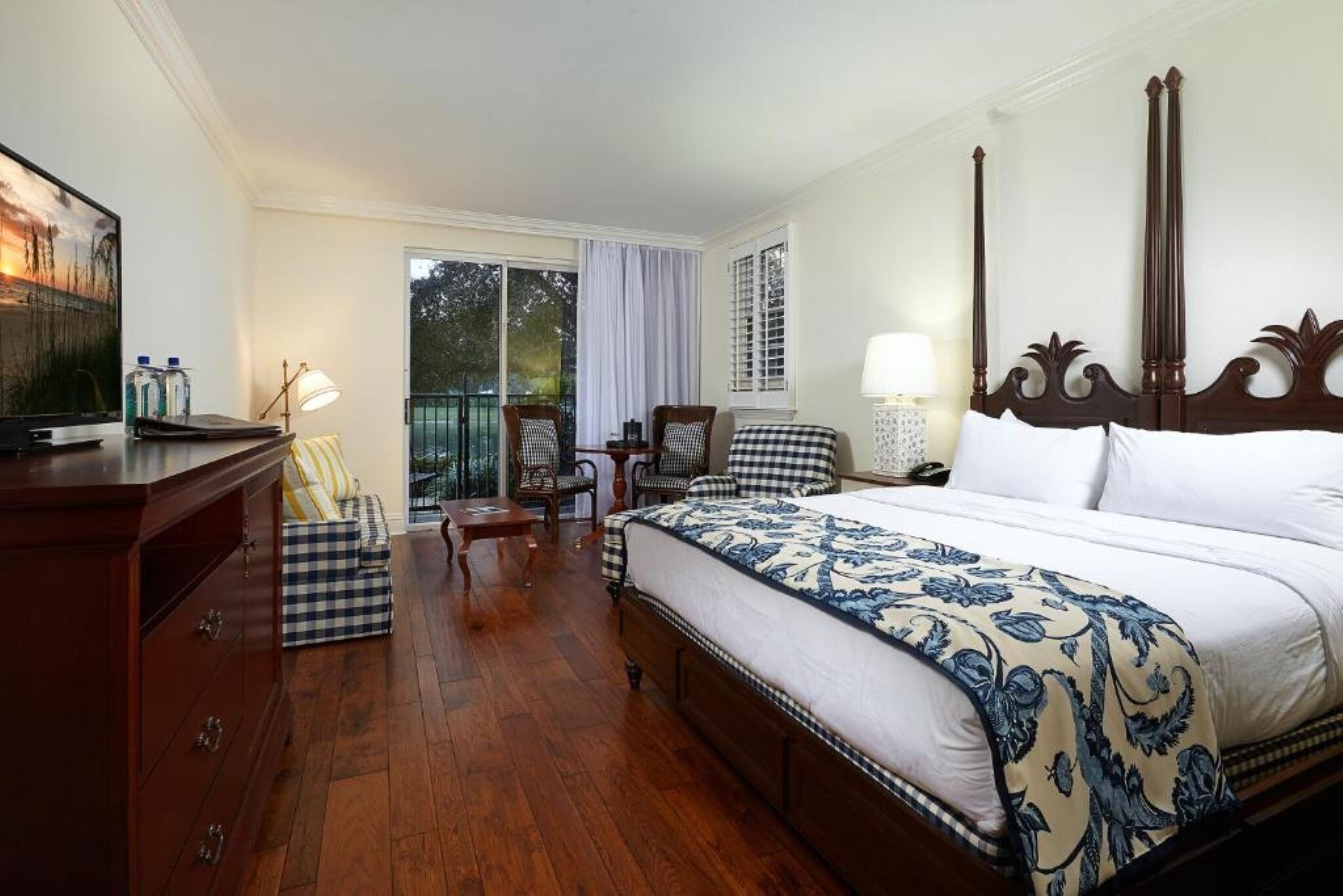 A hotel room with a large bed, a desk, a chair, a small table, and a balcony with a view.
