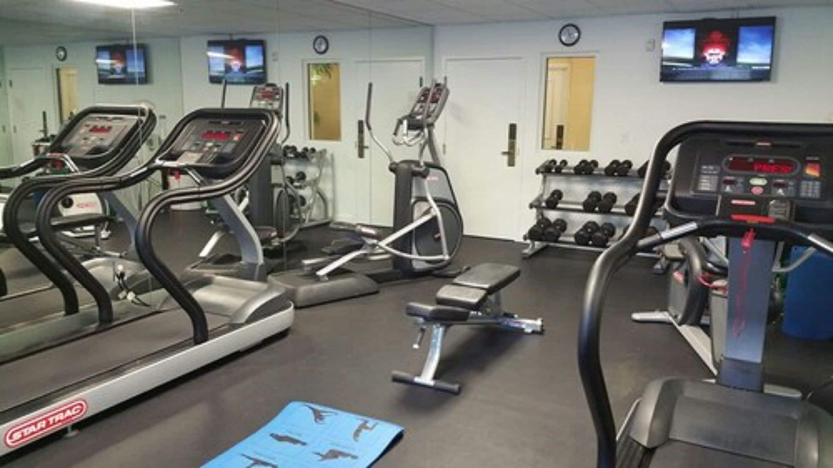 Une salle de sport équipée de tapis de course, d’un appareil elliptique et d’haltères.