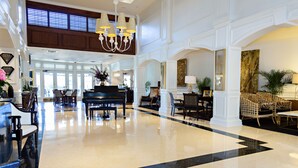 A spacious lobby with a grand piano, comfortable seating, and a polished floor.