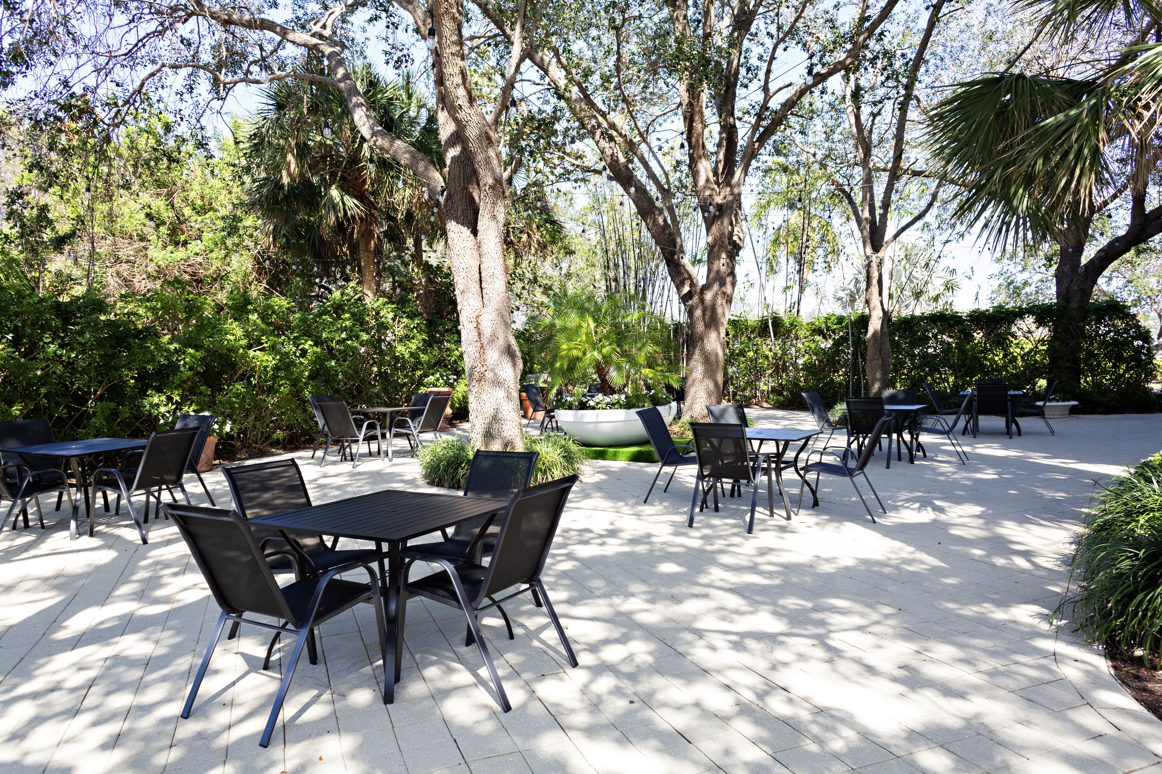 An outdoor patio with tables and chairs, surrounded by trees and greenery.