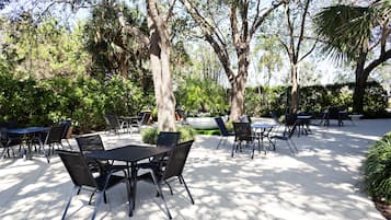 An outdoor patio with tables and chairs, surrounded by trees and greenery.