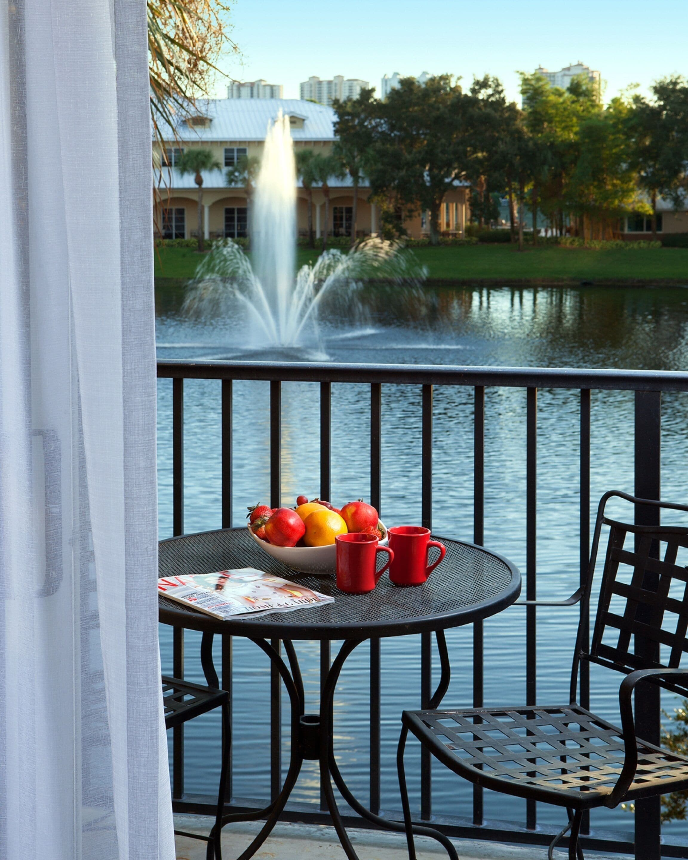 A balcony with a table set for two, a bowl of fruit, and two red cups.