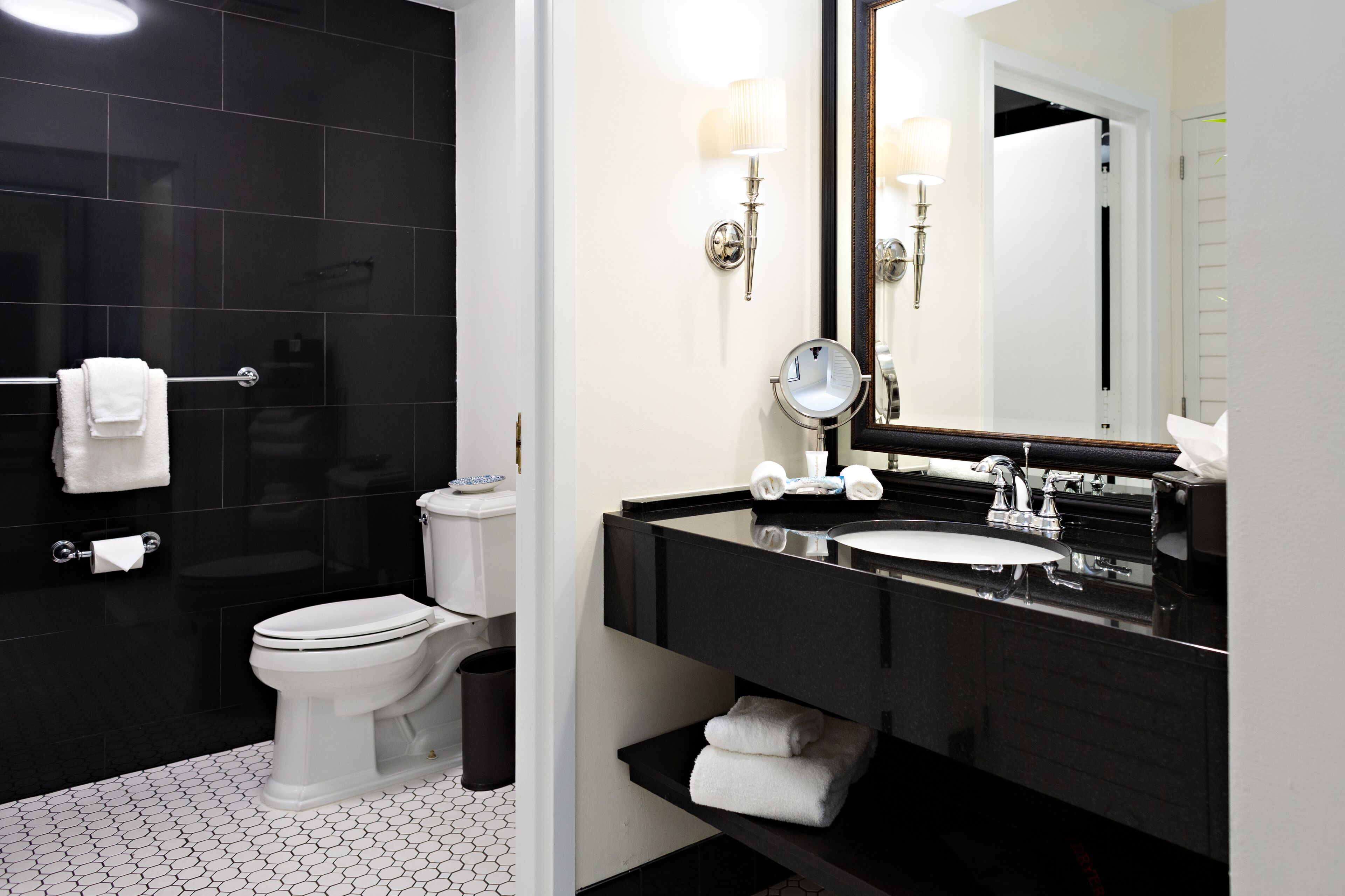 A modern bathroom with a black tiled shower, a white toilet, a black sink with a large mirror, and a white towel rack.