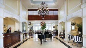 A spacious lobby with a grand piano, a reception desk, and a chandelier.