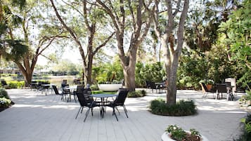 An outdoor patio area with tables and chairs, surrounded by trees and plants.