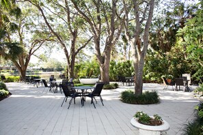 An outdoor patio area with tables and chairs, surrounded by trees and plants.