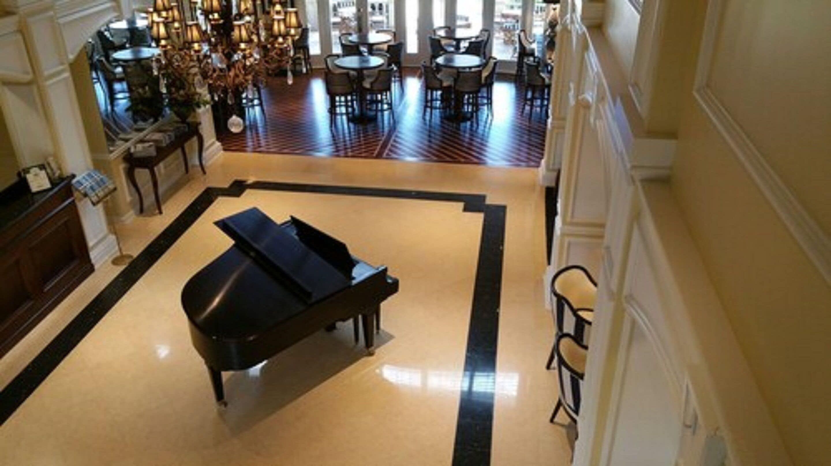 A grand lobby with a piano, a chandelier, and a seating area with tables and chairs.