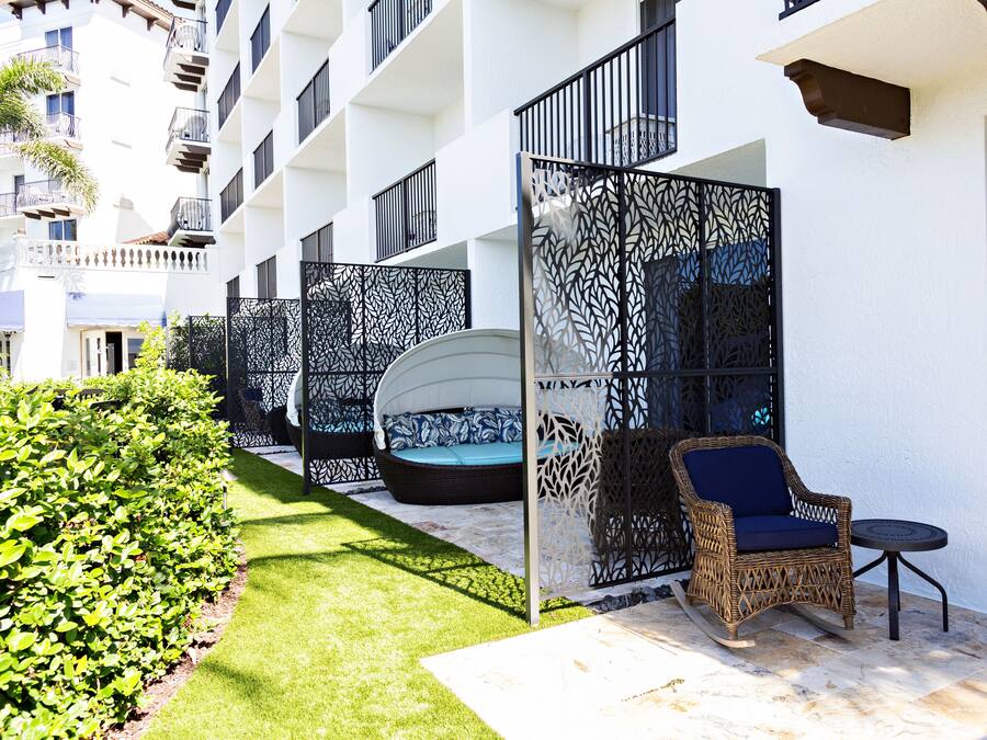 Un patio de hotel con un edificio blanco, mobiliario exterior con cojines y un césped bien cuidado.